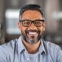 Smiling mature indian man wearing spectacles and looking at camera. Portrait of middle eastern confident businessman at office. Portrait of successful mid entrepreneur feeling satisfied and working from home.